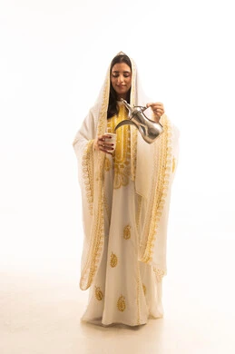 مفهوم الكرم وحسن الاستقبال، حب الوطن والانتماء اليه، ذكرى تأسيس الدولة السعودية الاولى 22 فبراير، يوم بدينا 1727 م،  بورتريه لشابة عربية خليجية سعودية ترتدي العباءة البيضاء المزخرفة تقوم بصب القهوة من الدلة النحاسية، الجسم بالطول الكامل، خلفية بيضاء