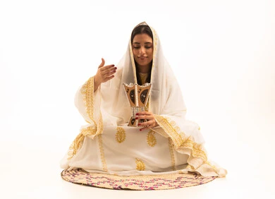 The use of oud wood in occasions and holidays, Saudi customs and traditions, the fragrance of incense and oud, a portrait of an Arab Saudi Gulf woman wearing a decorated abaya sitting on a straw mat holding a incense holder (mabkhara), white background.