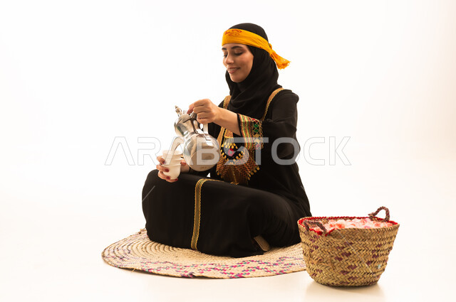 Love of the homeland and belonging to it, the anniversary of the establishment of the first Saudi state on February 22, the concept of generosity and good hospitality, the day we began in 1727 AD, a portrait of a Saudi Gulf Arab woman wearing a hijab, dressed in a shayla and a sidra, sitting on a straw mat pouring coffee from a brass dallah, white background.