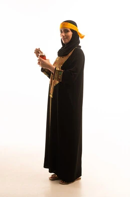 Healthy and beneficial food products made in Saudi Arabia, a side portrait of an Arab Gulf Saudi woman wearing the shayla and the sidra, holding a spoon dipped in natural honey in a glass container, on the day we started in 1727, wearing the traditional attire of the southern region, commemorating the founding of the Saudi state on February 22, expressions of pride and joy, full-body shot, white background.