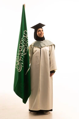 Pride and honor in symbols and the flag, the flags and national banners of Arab countries, a portrait of a Saudi Gulf Arab graduate wearing a white graduation gown and cap, holding the Saudi flag in her hands, the concept of love for the homeland and belonging to it, full-body, white background.