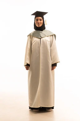 Standing upright and looking at the camera with gestures of pride and self-confidence, elegance and attention to appearance, university events and celebrations, a portrait of a Saudi Arabian Gulf female student wearing a white graduation gown and cap, full-body image, white background.