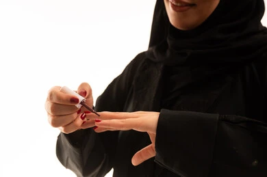 A Saudi expert in women's cosmetics, using a color for nail polish, a close-up portrait of a Saudi Gulf Arab woman wearing an abaya and hijab holding a manicure in her hand, the concept of caring for beauty and appearance, a women's beauty salon, white background.