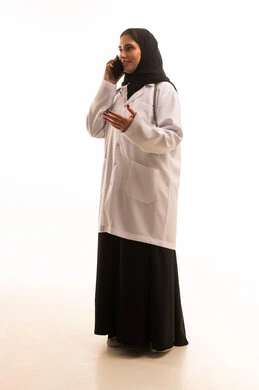 التواصل مع المرضى عبر الهاتف المحمول, مفهوم الطب والصحة، بورتريه لطبيبة عربية خليجية سعودية ترتدي المعطف الطبي تتحدث عبر الهاتف المحمول، الجسم بالطول الكامل، خلفية بيضاء