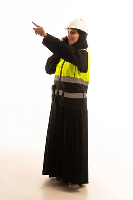 الاشارة الى شيء ما، استخدام جهاز تقني حديث متطور، مفهوم الهندسة والإنشاء المعماري, بورتريه لمهندسة عربية خليجية سعودية محجبة ترتدي العباءة والسترة و خوذة الحماية تمسك بيدها الهاتف المحمول، إجراء مكالمة صوتية، صورة الجسم بالطول الكامل، خلفية بيضاء