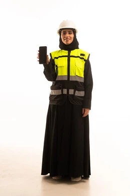 عرض الهاتف المحمول بشاشة سوداء فارغة، مفهوم الهندسة والإنشاء المعماري, بورتريه لمهندسة عربية خليجية سعودية محجبة ترتدي العباءة والسترة و خوذة الحماية تنظر الى الكاميرا تمسك بيدها الجوال، استخدام جهاز تقني حديث متطور، صورة الجسم بالطول الكامل، خلفية بيضاء