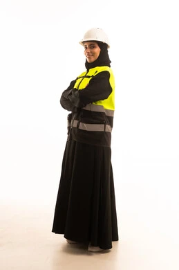The concept of engineering and architectural construction, a profession and job for women, a portrait of a veiled Saudi Gulf Arab engineer wearing an abaya and jacket and a safety helmet, standing with crossed arms looking with gestures of self-confidence, full-body image, white background.