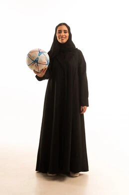 Practicing the hobby of football, passion for sports, a portrait of a young Arab Gulf Saudi woman wearing an abaya and hijab holding a ball with gestures of encouragement and enthusiasm, the Saudi women's team, a full-body image, white background.