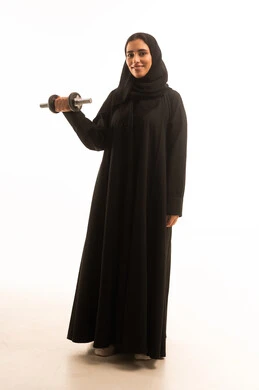 ممارسة التمارين الرياضية ورفع الاثقال مع الدمبل، بورتريه لشابة عربية خليجية سعودية محجبة ترتدي العباءة تحمل بيدها الأوزان الحديدية الثقيلة، المحافظة على الصحة واللياقة الجسدية والرشاقة البدنية،الجسم بالطول الكامل، خلفية بيضاء