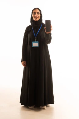 Electronic marketing and showcasing mobile applications, gestures of appreciation using modern technology, using smartphone applications, a portrait of a Saudi Gulf Arab woman wearing a hijab and an abaya, holding a white card with a blue ribbon and a mobile phone with a blank black screen, full-body image, white background. Electronic marketing and showcasing mobile applications, gestures of appreciation using modern technology, using smartphone applications, a portrait of a Saudi Gulf Arab woman wearing a hijab and an abaya, holding a white card with a blue ribbon and a mobile phone with a blank black screen, full-body image, white background.