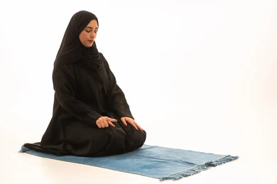 Worship and drawing closer to God, a Saudi girl performing the prayer obligation, the five pillars of Islam, a portrait of a young Arab Khaleeji Saudi woman wearing a hijab and abaya sitting on a designated prayer rug, white background.