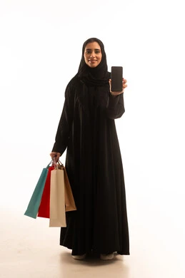 The use of technology in daily life, displaying a black screen on the mobile phone, shopping and purchasing supplies and gifts online, a portrait of an Arab Gulf Emirati woman wearing a hijab and abaya holding a mobile phone and shopping bags, looking at the camera with expressions of joy, full-body, white background.