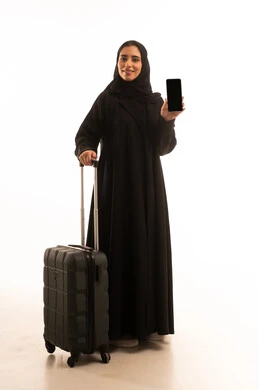 عرض شاشة سوداء فارغة عبر الهاتف المحمول، الذهاب في رحلة سفر، قضاء وقت ممتع بالاستماع الى الموسيقى, مفهوم الإصغاء والاستمتاع، استخدام الهيدفون في اوقات الفراغ، بورتريه لامرأة عربية خليجية سعودية ترتدي العباءة و الحجاب تمسك بيديها حقيبة السفر، الجسم بالطول الكامل، خلفية بيضاء