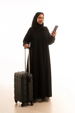 التجهيز للسفر والرحلات الممتعة، استخدام الأجهزة الحديثة و المتطورة , بورتريه لامرأة عربية خليجية سعودية محجبة ترتدي العباءة تمسك بيديها حقيبة السفر والهاتف المحمول, صورة للجسم بالطول الكامل , خلفية بيضاء