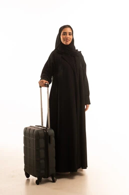 Looking at the camera with gestures of happiness and joy, enjoying sightseeing trips during the holiday, preparing for the summer vacation, getting ready for fun travels, a portrait of a Saudi Arabian Gulf woman wearing a hijab and an abaya holding a travel bag in her hand, full-body, white background.