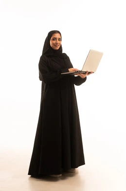 استخدام الأجهزة التقنية الحديثة والمتطورة، مفهوم العمل عن بعد, بورتريه لامرأة عربية خليجية سعودية محجبة ترتدي العباءة السوداء تعمل على جهاز الحاسوب المحمول, مفهوم إنجاز المهام , الجسم بالطول الكامل، خلفية بيضاء