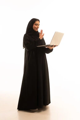 رفع كف اليد بتعابير التحية والسلام، اجراء مكالمات فيديو، التواصل مع الاهل والاصدقاء، انجازمهام العمل عن بعد، بورتريه  لامراة عربية خليجية سعودية محجبة ترتدي العباءة و الحجاب تعمل على جهاز الحاسوب، صورة لكامل الجسم، خلفية بيضاء