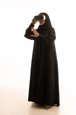 ارتداء نظارة الواقع الافتراضي، محاكاة العالم الخيالي, استخدام جهاز تقني حديث ومتطور للتسلية والترفيه, بورتريه لامراة عربية خليجية سعودية ترتدي الحجاب والعباءة تضع نظارات الفي ار ثلاثية الأبعاد على عينها, الجسم بالطول الكامل، خلفية بيضاء