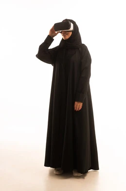 Simulation of a fantasy world, wearing virtual reality glasses, using a modern and advanced technical device for entertainment and amusement, a portrait of a Gulf Arab Saudi woman wearing a hijab and abaya, putting 3D VR glasses on her eyes, full-body, white background.