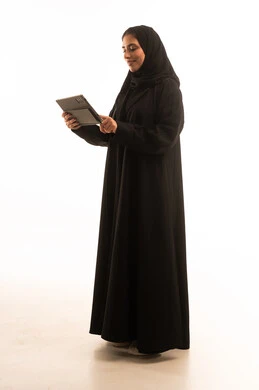 Integrating modern technology and technology into daily life, a portrait of a Saudi Gulf Arab woman wearing a hijab and abaya tapping on a tablet, browsing social media sites, a young Saudi woman working on the tablet, full-body image, white background.