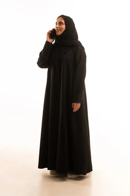 Spending enjoyable times exchanging news and conversations remotely, a portrait of a Gulf Arab Saudi woman wearing a hijab and an abaya, engaging in talks and chats with family and friends using a mobile phone, facial expressions indicating happiness and joy, full-body, white background.