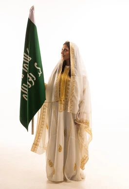 تأسيس الدولة السعودية الأولى 22 فبراير، ذكرى يوم بدينا 1727 م, بورتريه لإمرأة عربية خليجية سعودية ترتدي  العباءة المزخرفة تمسك راية وشعار يوم التأسيس بتعابير الفخر والاعتزاز, الجسم بالطول الكامل, خلفية بيضاء