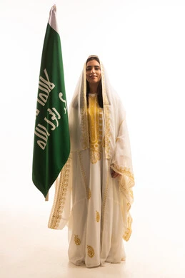 ذكرى يوم بدينا 1727 م، تأسيس الدولة السعودية الأولى 22 فبراير, بورتريه لإمرأة عربية خليجية سعودية ترتدي  العباءة المزخرفة تمسك راية وشعار يوم التأسيس بتعابير الفخر والاعتزاز, الجسم بالطول الكامل, خلفية بيضاء