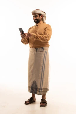 تصفح مواقع التواصل الاجتماعي، مفهوم التقنيات والأجهزة الحديثة، بورتريه لرجل عربي يمني يرتدي القميص والازار مع العمامة يحمل بيده الجوال، صورة الجسم بالطول الكامل، خلفية بيضاء