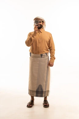 مفهوم توضيح الصورة، حب الاستكشاف والمغامرة, بورتريه لرجل عربي يمني يرتدي القميص والازار مع العمامة يحمل بيده عدسة مكبرة ينظر من خلالها, أدوات بصرية للرؤية عن قرب، مشاهدة الاشياء الصغيرة بدقة ووضوح, الجسم بالطول الكامل، خلفية بيضاء