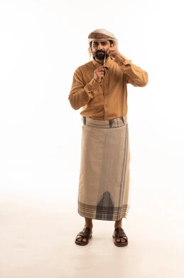 مفهوم العناية و الإهتمام بالجمال والمظهر الخارجي، بورتريه لرجل عربي يمني يرتدي القميص والازار مع العمامة يحمل بيده المقص ، قص و تصفيف الذقن في صالون الحلاقة، صالون حلاقة تجميلي رجالي ،الجسم بالطول الكامل، خلفية بيضاء