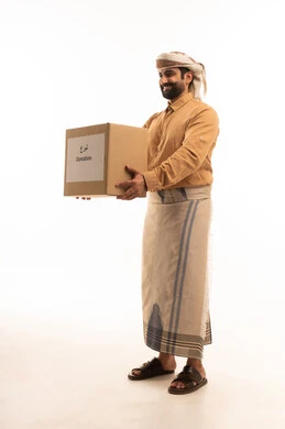 جمعية خيرية ومبادرة انسانية ، بورتريه لرجل عربي يمني يرتدي القميص والازار مع العمامة يحمل صندوق كرتوني ، توفير المستلزمات الضرورية للفقراء، مفهوم المساعدة والتبرع، الجسم بالطول الكامل، خلفية بيضاء