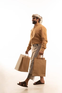 التبضع وأخذ الحاجات اللازمة, المشتريات التجارية والهدايا, الاستفادة من الحسومات والتصفيات, بورتريه من الجانب لرجل عربي يمني يرتدي القميص والازار مع العمامة يمسك بيده أكياس ورقية ملونة, الجسم بالطول الكامل, خلفية بيضاء