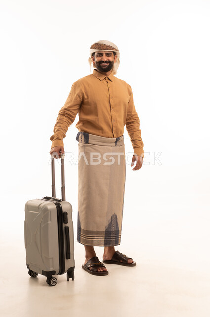 Going on recreational tours, preparing for an enjoyable summer trip, the concept of tourism during the summer vacation, gestures of joy and happiness, a portrait of a Yemeni Arab man wearing a shirt and a sarong with a turban holding a suitcase in his hands, full-body, white background.