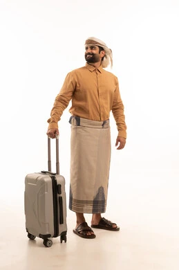 التحضير لقضاء رحلة صيفية ممتعة، مفهوم السياحة في إجازة الصيف، ايماءات السرور والفرح، القيام بالجولات الترفيهية، بورتريه لرجل عربي يمني يرتدي القميص والازار مع العمامة يمسك بيدية حقيبة الامتعة, الجسم بالطول الكامل، خلفية بيضاء