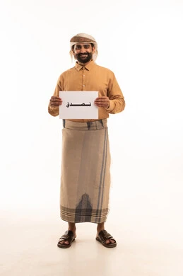 الأعمال الخيرية الإسلاميه، المساعدات والتبرعات الإنسانية، بورتريه لرجل عربي يمني يرتدي القميص والازار مع العمامة  يحمل بيده موك اب مربع أبيض مكتوب عليه تصدق، صورة الجسم بالكامل، خلفية بيضاء