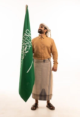 إحياء ذكرى اليوم الوطني السعودي 23 سبتمبر، يوم العلم السعودي 11 مارس, إيماءات الفخر و السرور بالانتماء للوطن, بورتريه لرجل عربي يمني يرتدي القميص والازار مع العمامة يحمل بيده علم المملكة، يوم بدينا 1727 م، الجسم بالطول الكامل، خلفية بيضاء