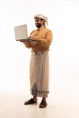 Integrating work with technology, managing and organizing work affairs through technical devices, a portrait of an Arab Yemeni man wearing a shirt and a waist wrap with a turban working on a laptop, remote work and completing required tasks, full-body, white background.