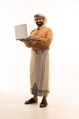 إدارة شؤون العمل وتنظيمه عبر الاجهزة التقنية، مهنة ووظيفة ادارية، دمج العمل مع التكنولوجيا، بورتريه لرجل عربي يمني يرتدي القميص والازار مع العمامة يعمل على الحاسوب المحمول، العمل عن بعد وانجاز المهام المطلوبة، الجسم بالطول الكامل، خلفية بيضاء