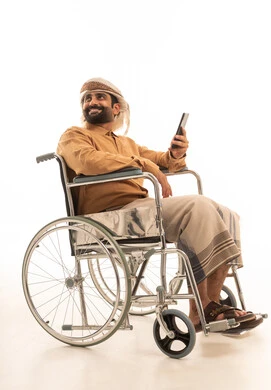 مشاهدة الأفلام والمسلسلات الممتعة، متابعة مواقع التواصل الاجتماعي عبر الهاتف المحمول، التواصل مع الأهل والأصدقاء، استخدام التكنولوجيا و التقنيات الحديثة,  بورتريه لرجل عربي يمني يرتدي القميص والازار مع العمامة يجلس على كرسي متحرك يحمل بيده موبايل، خلفية بيضاء