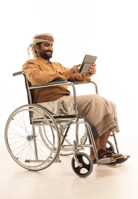 Chatting with family and friends, expressions and gestures of integration and joy, using advanced modern technology in professional life through a tablet, a portrait of a Yemeni Arab man wearing a shirt and a waist wrap with a turban sitting in a wheelchair working on a tablet, white background.
