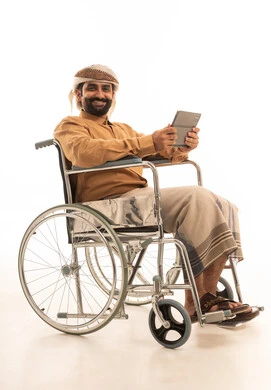 تعابير وايماءات الاندماج و السرور، استخدام التقنية الحديثه المتطورة في الحياة العملية عبر الجهاز اللوحي، بورتريه لرجل عربي يمني يرتدي القميص والازار مع العمامة يجلس على كرسي متحرك  يقوم بالعمل على جهازالتابلت، خلفية بيضاء