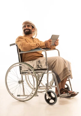 النظر الى شيء ما، تعابير وايماءات الاندماج و السرور، استخدام التقنية الحديثه المتطورة في الحياة العملية عبر الجهاز اللوحي، بورتريه لرجل عربي يمني يرتدي القميص والازار مع العمامة يجلس على كرسي متحرك  يقوم بالعمل على جهازالتابلت، خلفية بيضاء