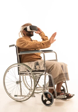 Raising the palm of the hand upwards with gestures of integration and simulating the imaginary world, wearing 3D VR glasses, technological and technical evolution, a portrait of a Yemeni Arab man wearing a shirt and a waist wrap with a turban sitting in a wheelchair looking through virtual reality glasses, white background.