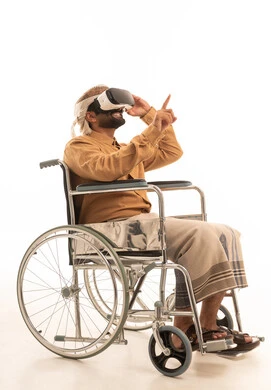 Referring to something, the immersion and simulation of the imaginary world, the enjoyment and entertainment of watching through virtual reality glasses, a portrait of an Arab Yemeni man wearing a shirt and a waist wrap with a turban sitting in a wheelchair wearing 3D glasses (VR), technological and technical development, white background.