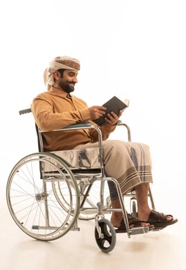 Spending time reading, learning, and culture, the concept of contemplation and focus, a portrait of an Arab Yemeni man wearing a shirt and a sarong with a turban sitting in a wheelchair holding a book in his hands, white background.