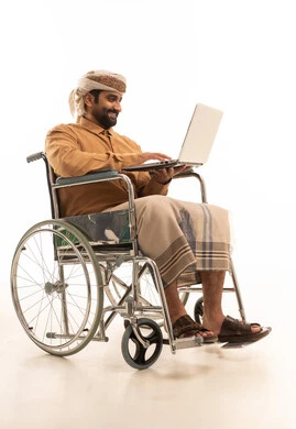 إدارة شؤون الأعمال وتنظيمها عبر الاجهزة التقنية، بورتريه لرجل عربي يمني يرتدي القميص والازار مع العمامة  يجلس على كرسي متحرك يستخدم الحاسب المحمول , خلفية بيضاء