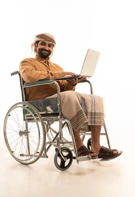 The concept of remote work, social media slaps, a portrait of an Arab Yemeni man wearing a shirt and a sarong with a turban sitting in a wheelchair using a laptop, white background.