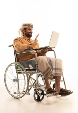 اجراء مكالمة فيديو، رفع كف اليد بتعابير التحية و السلام، بورتريه لرجل عربي يمني يرتدي القميص والازار مع العمامة  يجلس على كرسي متحرك يستخدم الحاسب المحمول , خلفية بيضاء