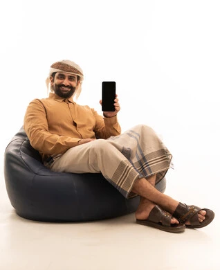 A blank black screen displayed on the mobile, gestures of happiness and joy, a portrait of a Yemeni Arab man wearing a shirt and a sarong with a turban sitting on a chair holding a mobile phone in his hands, white background.