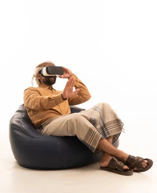 التفاعل مع العالم الخيالي، التطور التقني والتكنولوجي، المتعة والتسلية بالمشاهدة عبر نظارة الواقع الافتراضي، بورتريه لرجل عربي يمني يرتدي القميص والازار مع العمامة يجلس على كرسي بين باج يضع نظارة ثلاثية الأبعاد (الفي ار)، خلفية بيضاء